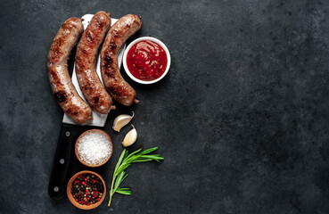 grilled sausages over meat knife with spices and rosemary on a stone background with copy space for...