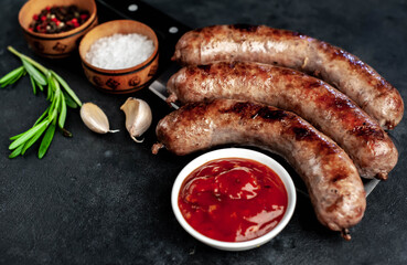 grilled sausages over meat knife with spices and rosemary on a stone background
