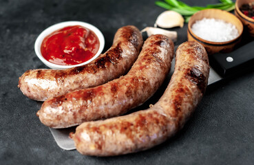 grilled sausages over meat knife with spices and rosemary on a stone background