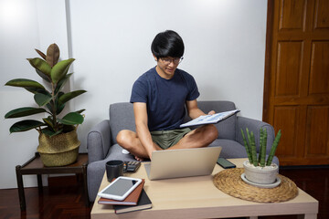 handsome asian freelancer sitting on the cozy working on his laptop computer remotely from home