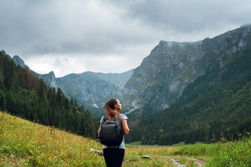 Rear shot of young brunette backpacker woman hiking on the green pathway in Tatra Mountains to Rysy...