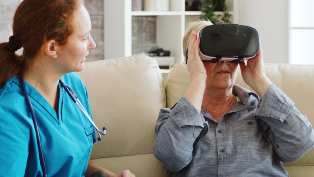 Female nurse helping senior woman to experience virtual reality with vr goggles in nursing home