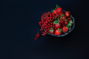 Vase with red strawberries and red currants on a black background view from the top.