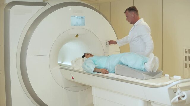 Magnetic resonance imaging, adult man doctor performs a magnetic tomographic examination of a young asian woman, MRI, modern technologies in medicine.