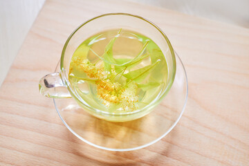 Transparent glass cup of herbal tea with linden flowers on a wooden background