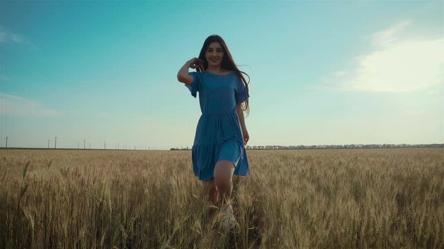 Young woman runs across field. Beautiful free girl enjoying nature in warm sunshine in wheat on sunset background. Happy and successful lifestyle concept