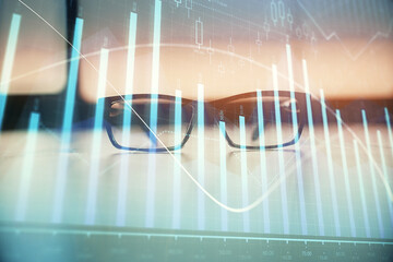 Financial graph hologram with glasses on the table background. Concept of business. Double exposure.