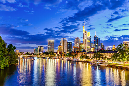 Frankfurt am Main. European finance center city downtown skyline cityscape. Eiserner steg bridge, river during twilight blue hour, sunset, evening, night. Gold yellow color. Travel in Hesse, Germany.
