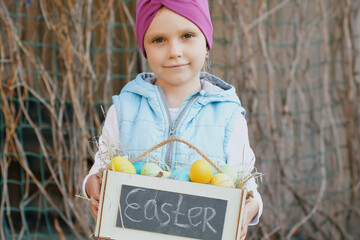 Portrait of cute smiling girl holding wooden planter with multi colored easter eggs and looking at camera