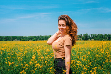 Portrait of a smiling young girl with long hair in a thick rapeseed field with a blue clear sky, place for text, copyspace