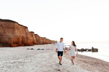Loving couple in white clothes during a honeymoon at sea walk on the sand at a photoshoot Love Story, ocean coast, beach