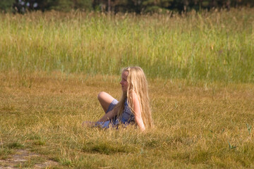 Mädchen im Kleid mit blonden langen Haaren sitzt auf einer Wiese