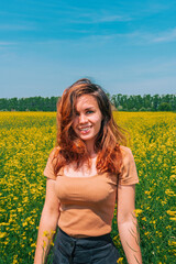 Naklejka na ściany i meble Portrait of a smiling young girl with long hair in a thick rapeseed field with a blue clear sky, place for text, copyspace