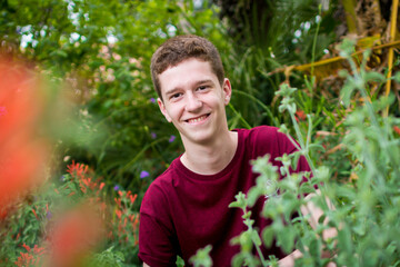 Red-haired teenager looking between plants in a purple shirt.