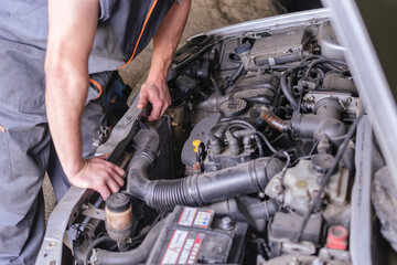 Mechanic in working overalls looking at a car engine.