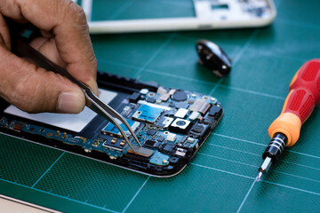 Technician man hand repairing and  assembling the motherboard of mobile smart phone by using soldering and forceps in lab room .Maintenance concept.