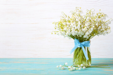 bouquet of lilies of the valley in a vase with blue ribbon on a blue white wooden background