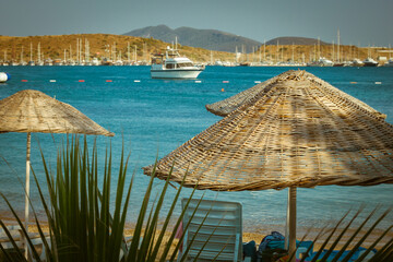 Thatched sun umbrellas, beach umbrellas on the sea background with blurred yachts