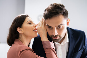 Woman Whispering Gossip In Friend's Ear At Workplace