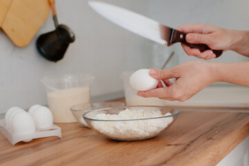 Cheese pancakes. The process of making cheesecakes in the home kitchen. A bowl of cottage cheese, a woman pours the cottage cheese into a bowl and drives an egg. Cottage cheese and yolk.