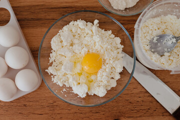 Cheese pancakes. The process of making cheesecakes in the home kitchen. A bowl of cottage cheese, a woman pours the cottage cheese into a bowl and drives an egg. Cottage cheese and yolk.