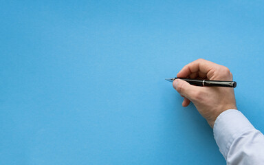 Man hand about to write on blank blue background. Male hand writing on a blank surface with black...