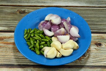 Pile of green chilly, peeled garlic and shallot on the plastic plate. Main ingredients in Thai cuisine. Preparation spices dipping sauce in Asia kitchen.