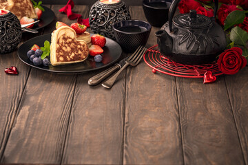 Valentine's day background with delicious pancakes in form of heart, green tea, black teapot, candles and roses. Valentines day concept greeting card. Copy space.