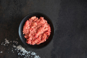 Homemade minced meat in a black bowl and salt on a black background. Fresh Raw mince. Top view with...