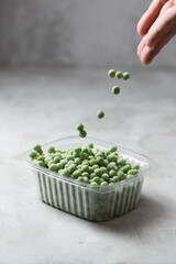 Falling frozen green peas in the storage box on the kitchen table, vertical orientation