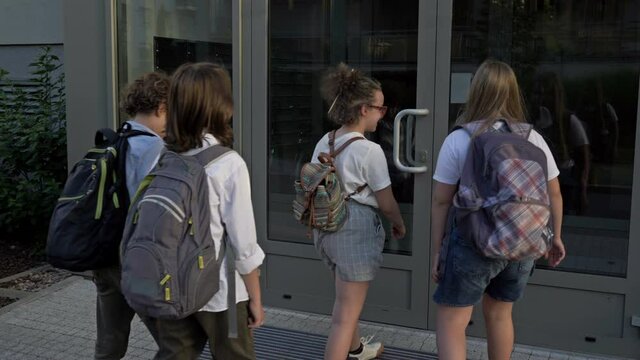 Four teenagers with backpacks enter the school building. Back to school.
