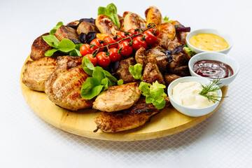 plate with fried meat, a wooden plate on a white tablecloth with fried meat, steak, barbecue, tomatoes and sauce