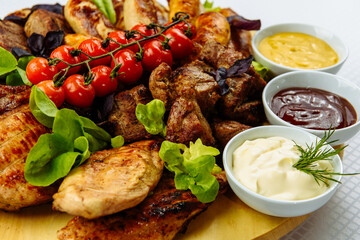 plate with fried meat, a wooden plate on a white tablecloth with fried meat, steak, barbecue, tomatoes and sauce