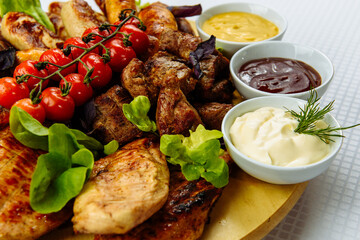 plate with fried meat, a wooden plate on a white tablecloth with fried meat, steak, barbecue, tomatoes and sauce