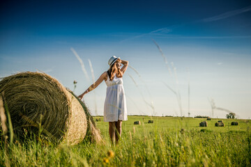 Beautiful girl is resting after work. girl on the field with hay. Woman near a sheaf of hay in a field. Rural life. Holidays in the village
