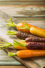 Fresh raw colorful carrots roots, purple, yellow and orange on old wooden table. Healthy food vegetable background with copy space. Toned photo.