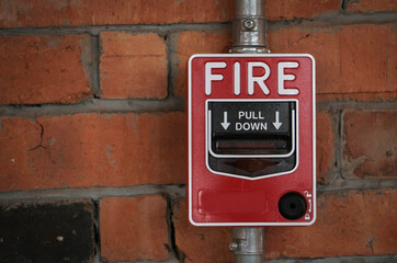 Red manual pull fire alarm safety system on brick wall.