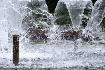Selective focus on spray of urban fountain and blurred background. A fountain with splashes and drops of water works. Abstract image of a jet of water in a fountain. Frozen motion. Copy space.