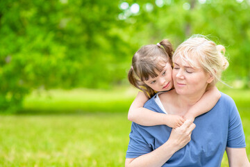 Fototapeta premium Portrait of a mother and little girl with special needs in summer park. Empty space for text