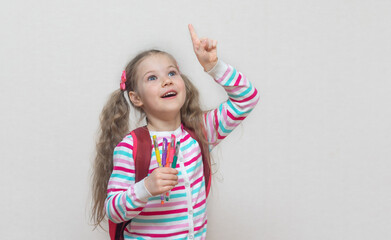 Back to school. Portrait of a blonde schoolgirl in a jacket with colored gel pens in her hands. The girl smiles and looks up. Thumbs up. Light background. Education. copy place.