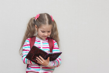 Back to school. A portrait of a fair-haired schoolgirl stands with a notebook in her hands and writes in it. Light grey Studio background. Education. copy place