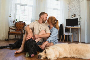 young couple with dogs sitting on the floor of their flat and having fun. dogs playing with their toys. man and woman kiss each other and spend leisure  time with their dogs