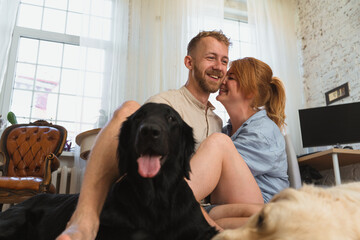 young couple with dogs sitting on the floor of their flat and having fun. man and woman hug each other and spend leisure  time with their dogs