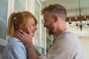 young couple kissing sitting on the kitchen table in their flat. happy couple smiling. young redhead woman and man