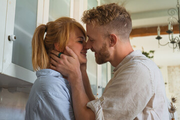 young couple kissing sitting on the kitchen table in their flat. happy couple smiling. young redhead woman and man