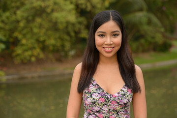 Portrait of happy young beautiful Asian woman smiling at the park