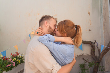 young couple is spending time on a balcony of their flat.  couple smiling and spending leisure time together. man and woman holding each other and kiss on the balcony