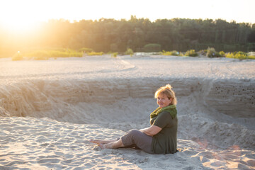 happy senior woman sitting on a sand outside in summer