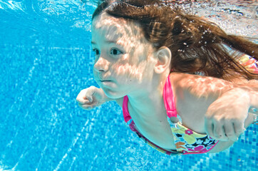 Child swims underwater in swimming pool, little baby girl dives and has fun under water, kid...