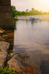 Obraz premium Stone shore in town in focus, blue fishing boat out of focus in the background. Warm summer day, Soft sun flare.